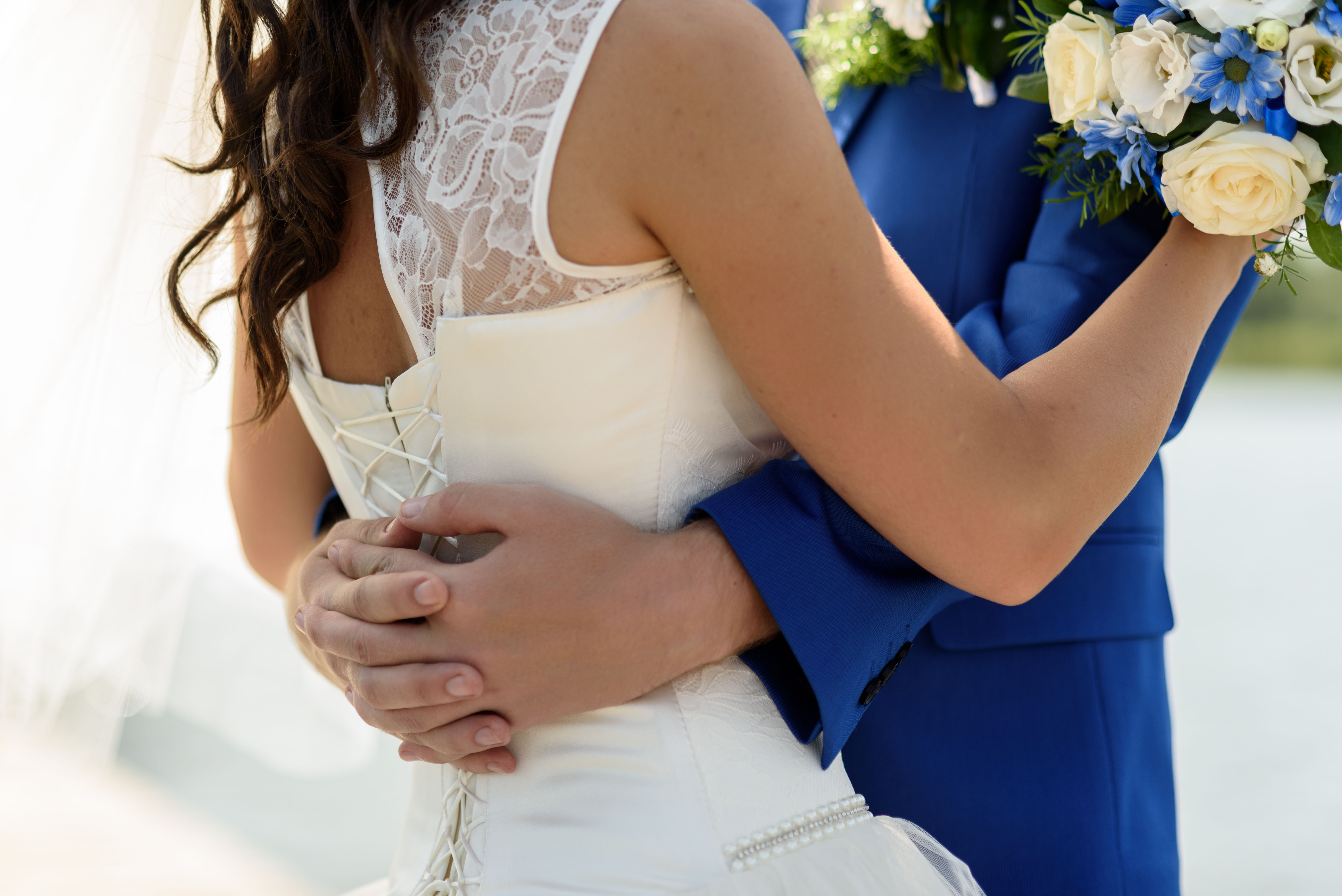 The torsos of a couple dressed in wedding attire hugging.